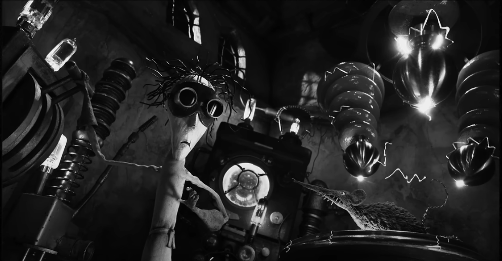 Black and white screenshot of an animated stop-motion scene inside a lab where the main foregrounded character wears goggles.